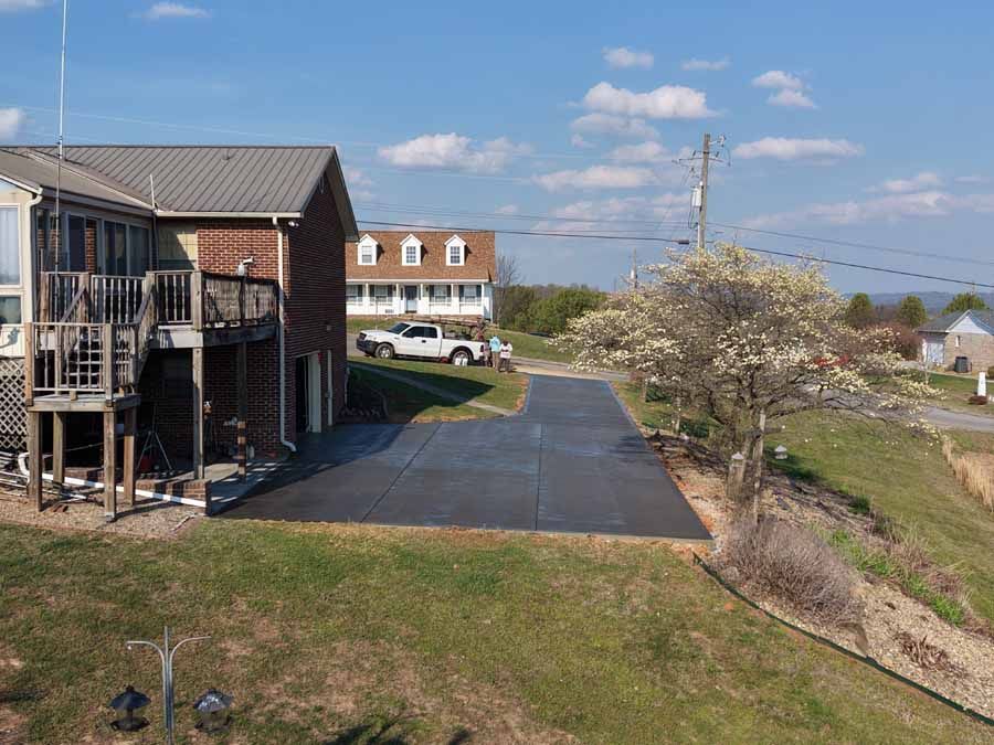 Apartment building with balconies beside a long paved driveway and grassy embankment under a blue sky