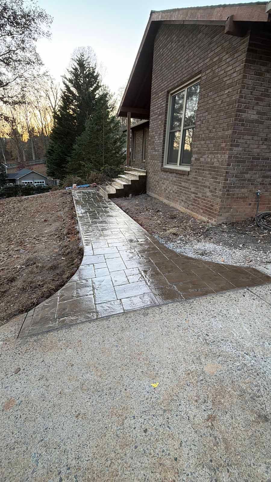 Brick house with a wet stone walkway and steps leading through a landscaped yard at dusk