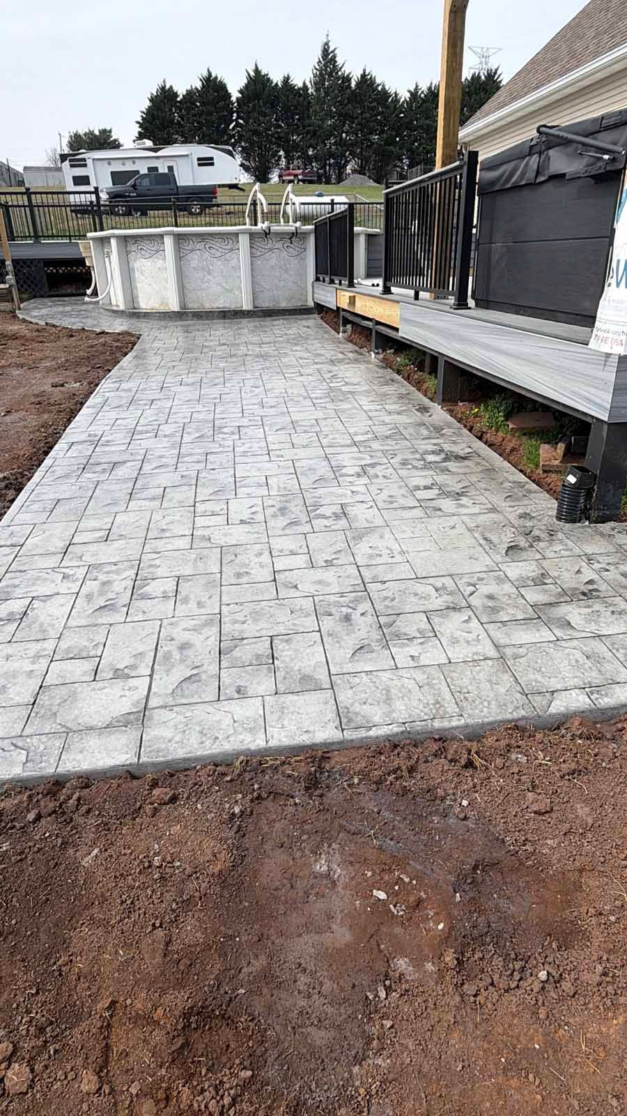 New stone paver walkway beside a house, with dirt edges and a fenced yard in the background