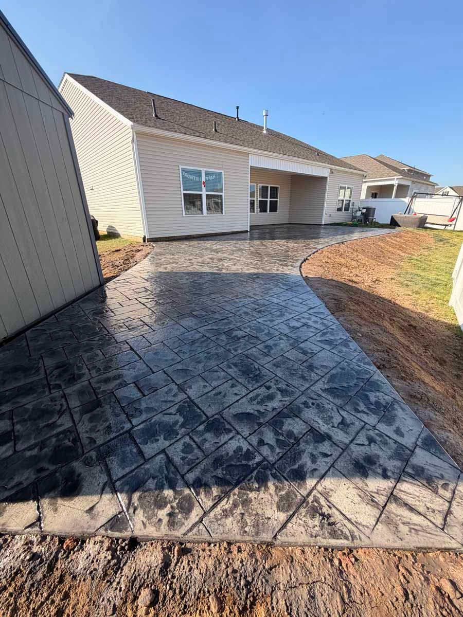 Stamped concrete backyard patio beside a beige house with windows and a small grassy yard