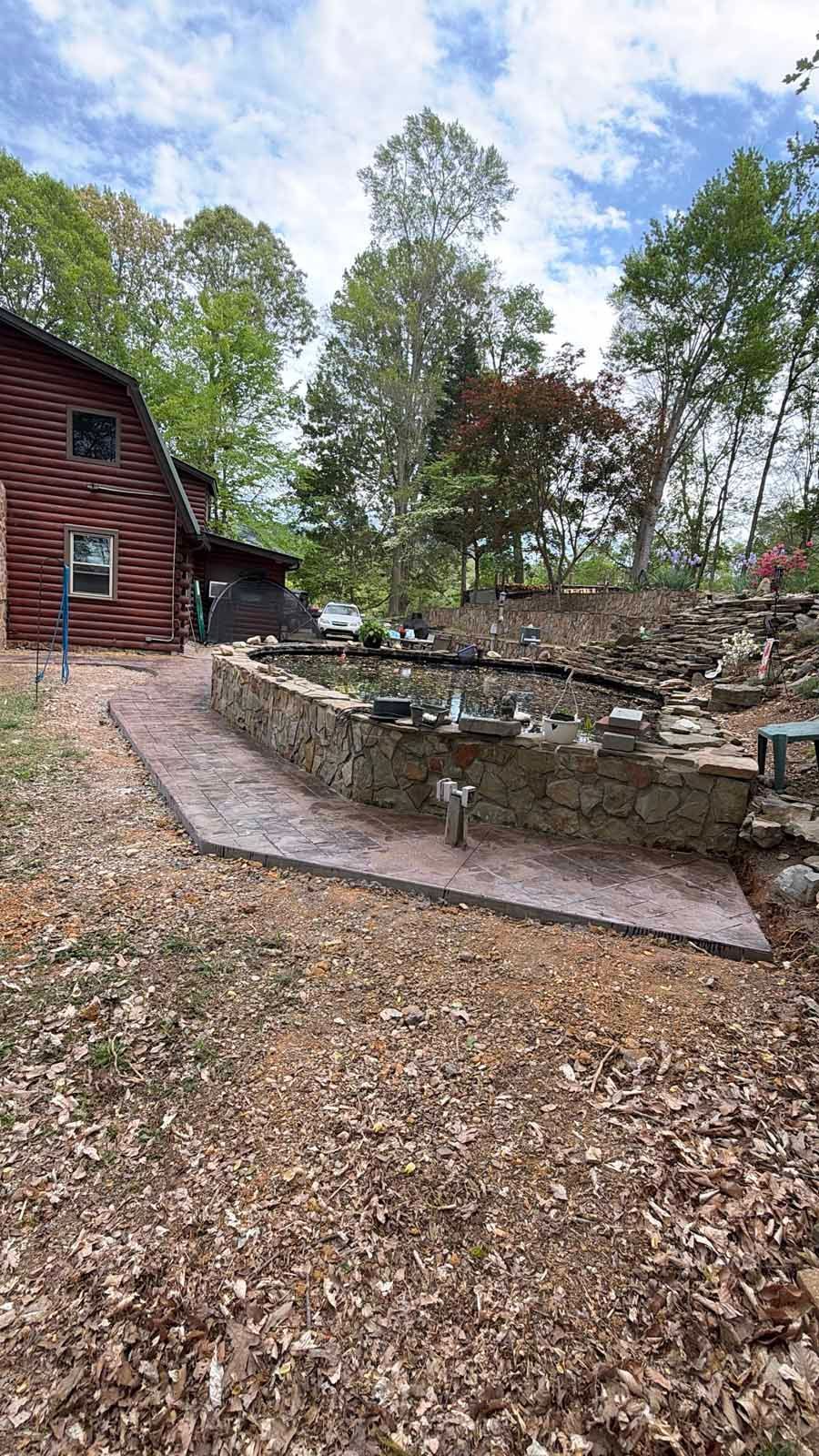 Curved stone garden bed beside a red wooden cabin, with a gravel path and tall trees under a cloudy sky