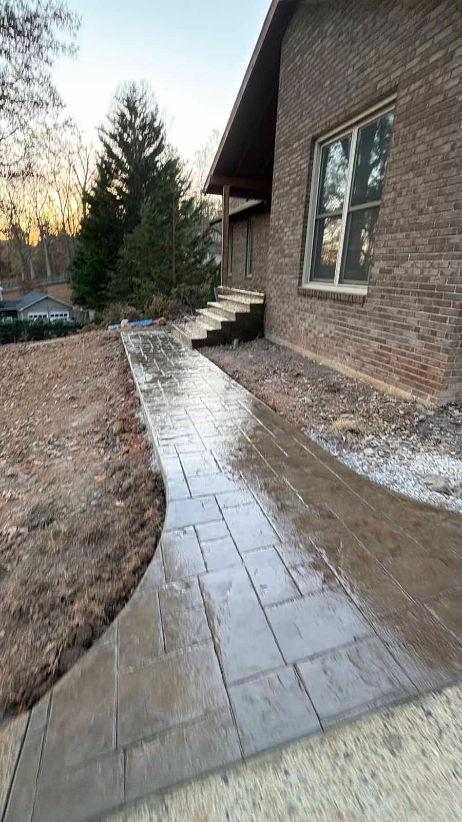 Brick house exterior with a narrow wet stone walkway and a snow-dusted yard beside it