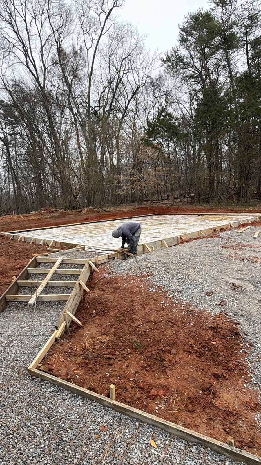 Worker pouring gravel on a new concrete and red-mulch landscape area near a wooded yard