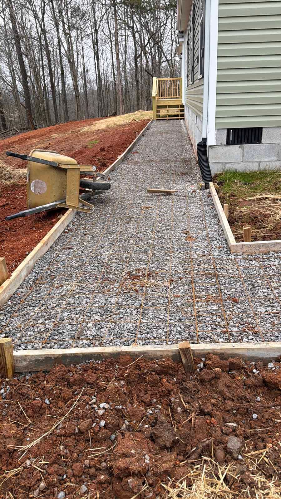 Gravel walkway under construction beside a house, with wooden forms and red soil edging.