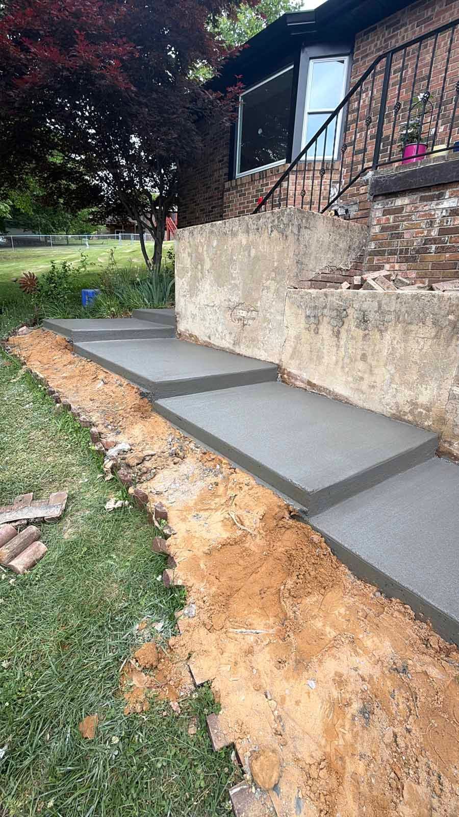 Fresh concrete walkway beside a brick house, bordered by dirt and grass