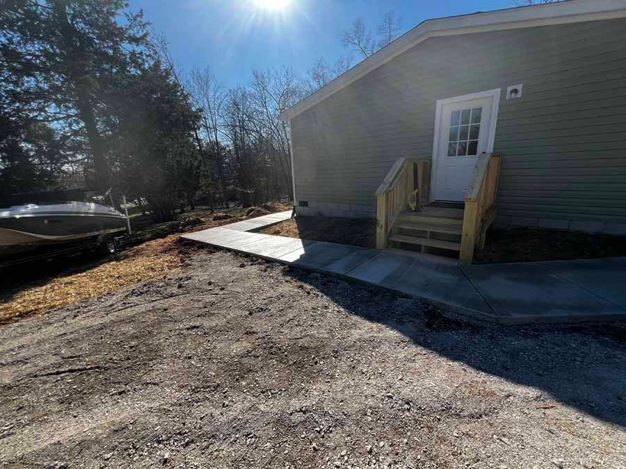 Sunlit gravel driveway beside a gray house with a small wooden porch and parked car