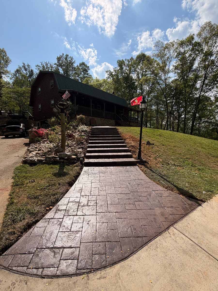 Stone walkway leads to cabin entrance with steps, landscaped slopes, and a red flag under a blue sky