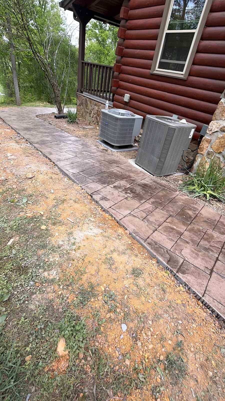Stone walkway beside a log cabin with two outdoor AC units and a gravel yard.