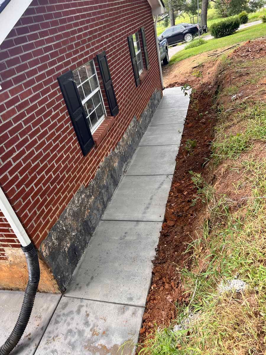 Concrete walkway beside red brick house with black shutters and mulch border