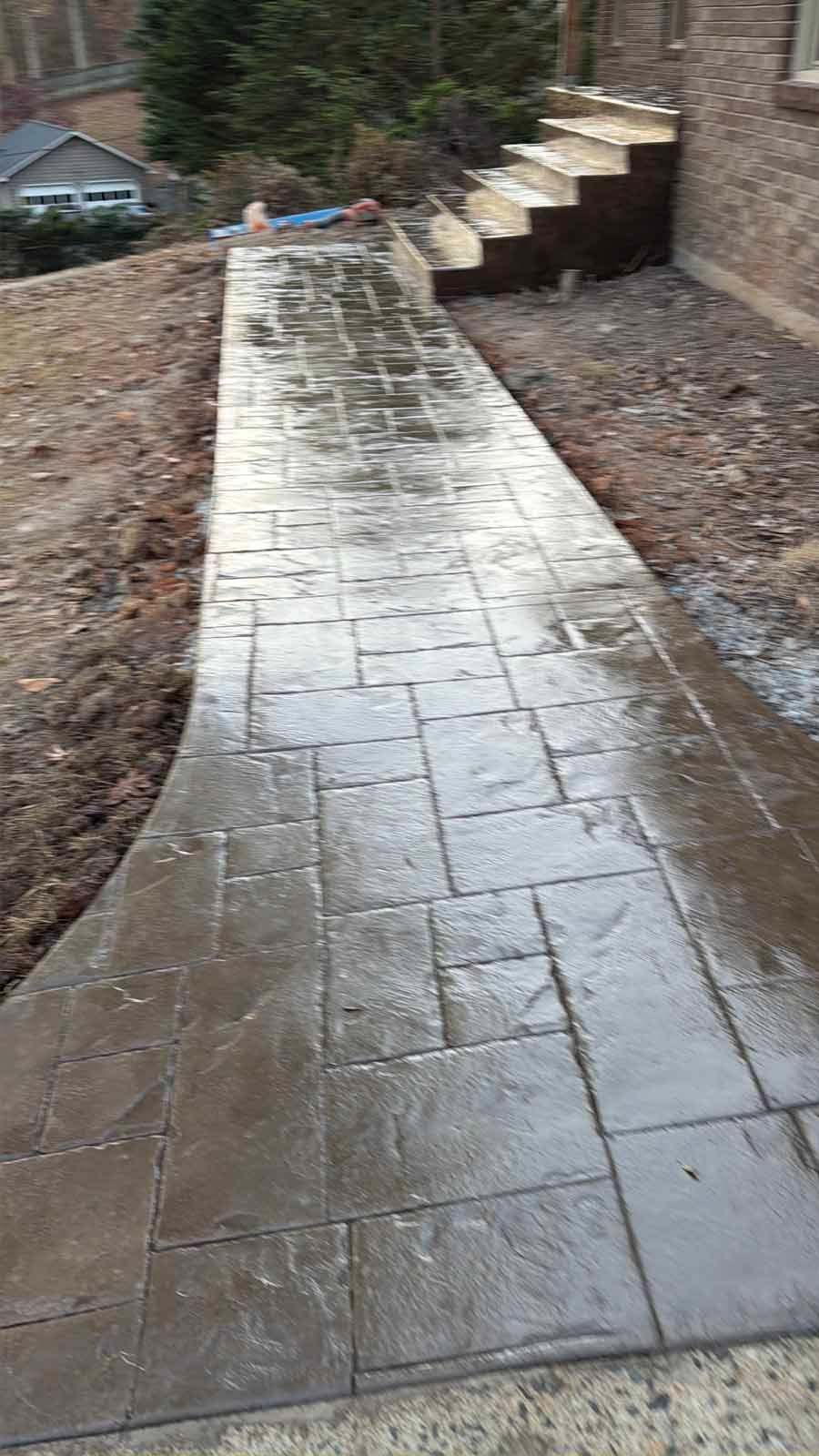 Wet concrete walkway leading up to stone steps beside a brick house.