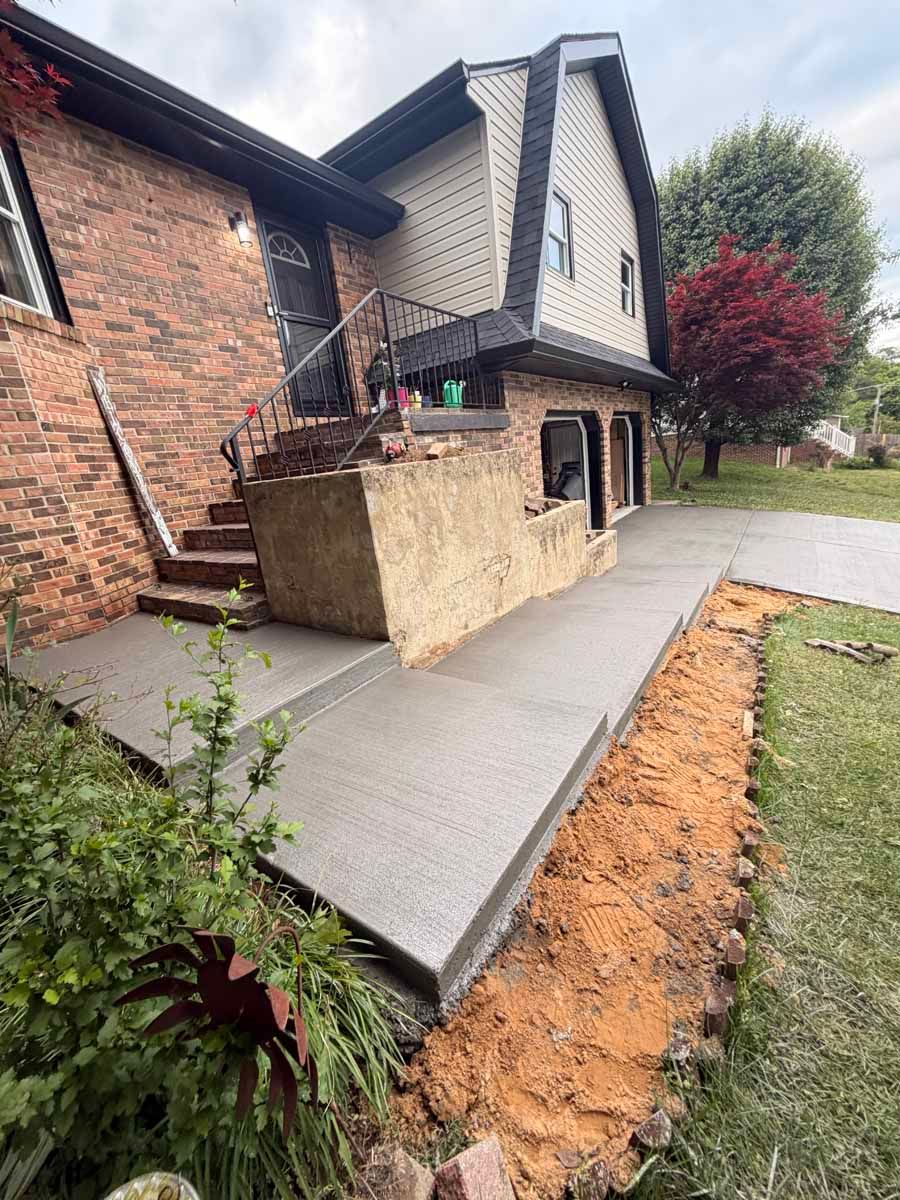 House exterior with newly poured concrete ramp beside brick walls and landscaping