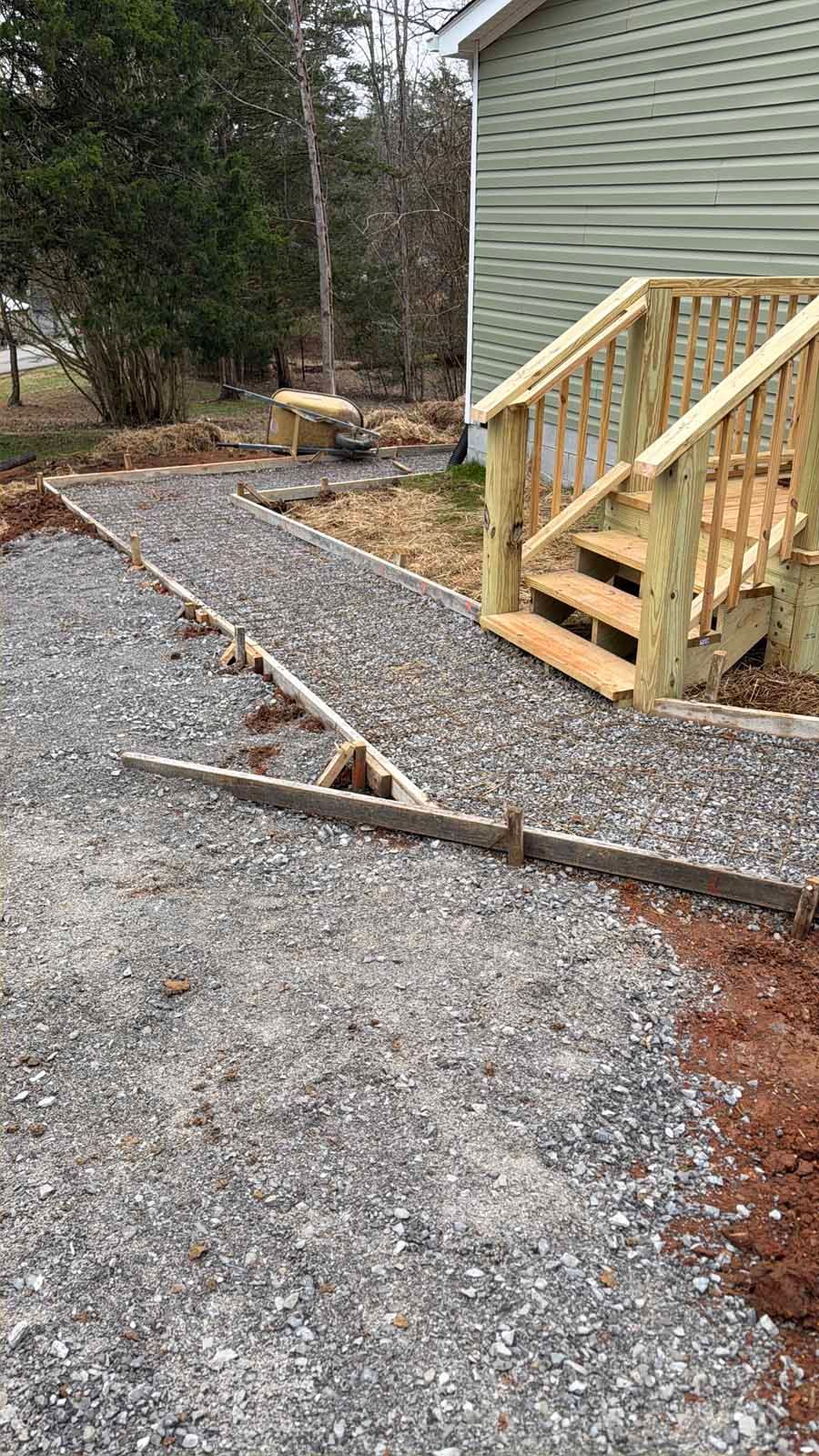 Gravel driveway beside a house, with a wooden wheelchair ramp and stairs under construction.