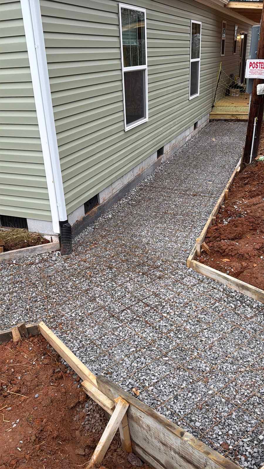 Gravel walkway beside a house with white-trimmed windows and a wooden border under construction