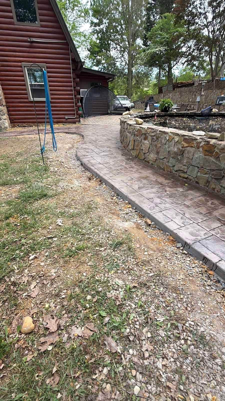 Stone walkway beside a log cabin and retaining wall in a wooded yard