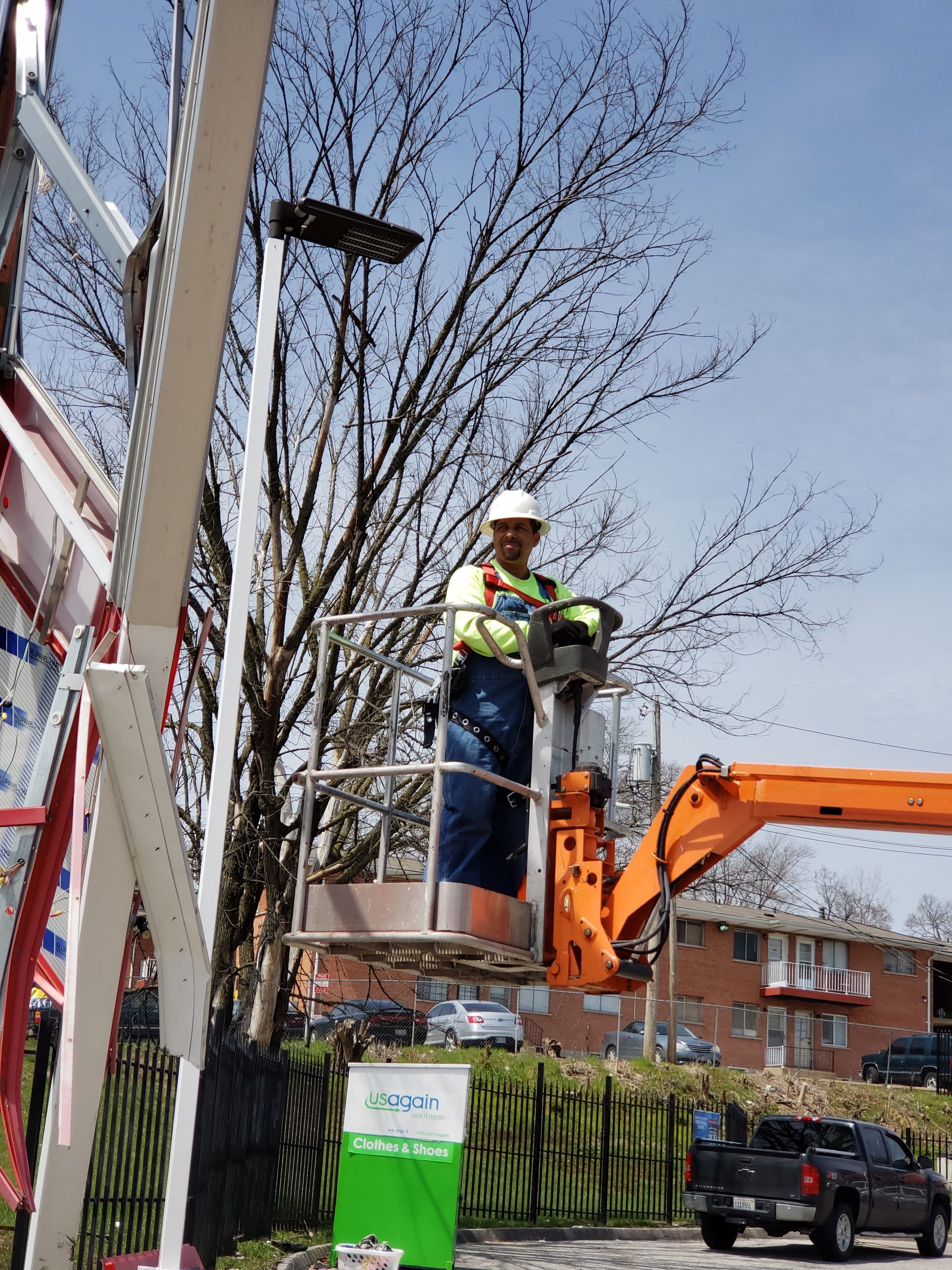 A man is sitting in a bucket on top of an orange crane.