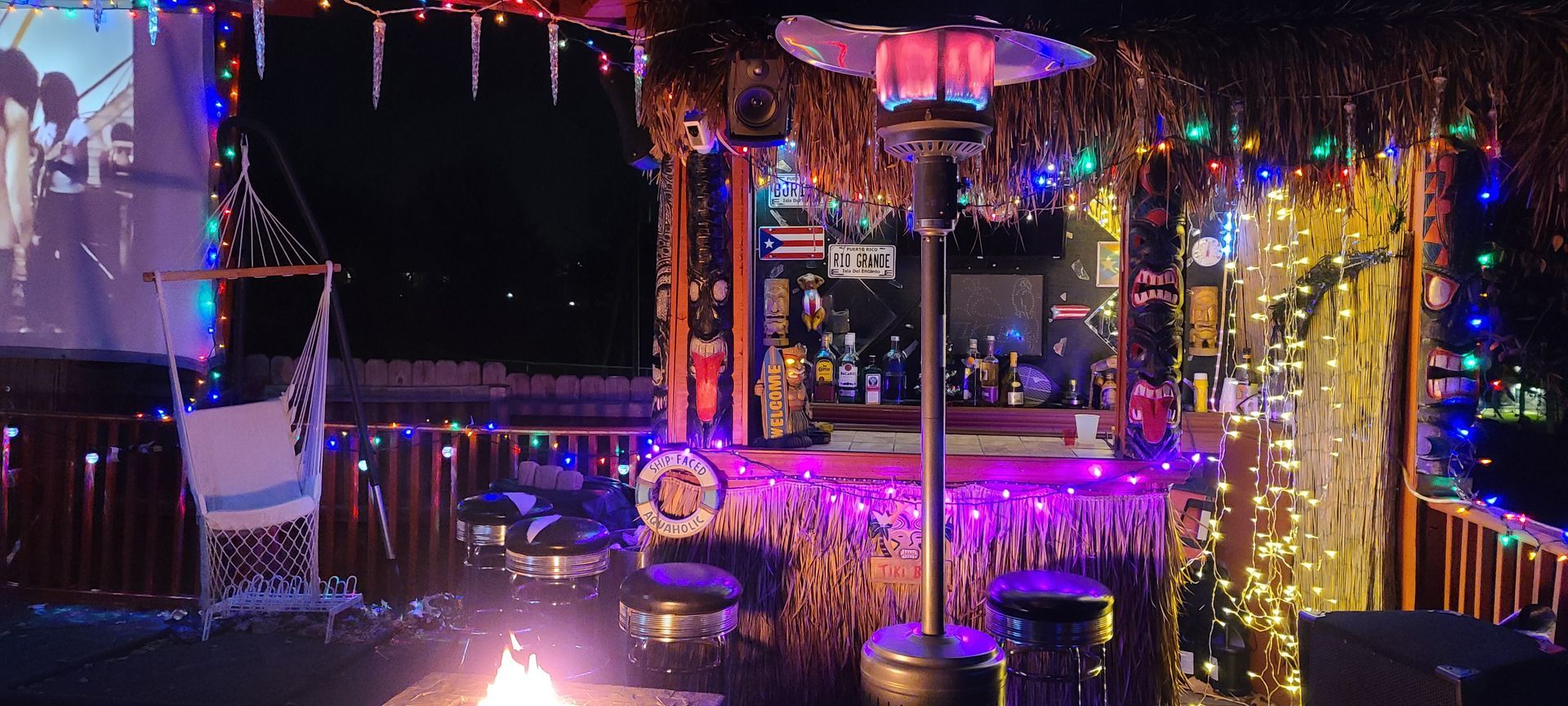 A fire pit is in front of a bar decorated with christmas lights.