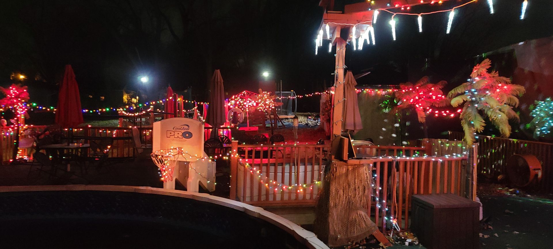 A swimming pool decorated with christmas lights and umbrellas at night.