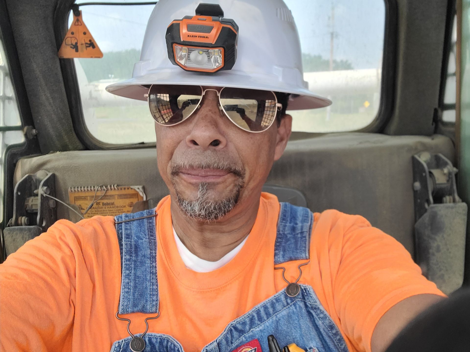 A man wearing overalls and a hard hat is taking a selfie