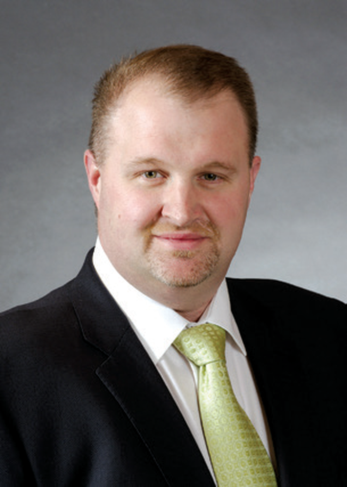 Portrait of a man in a dark suit and light green tie against a gray studio background
