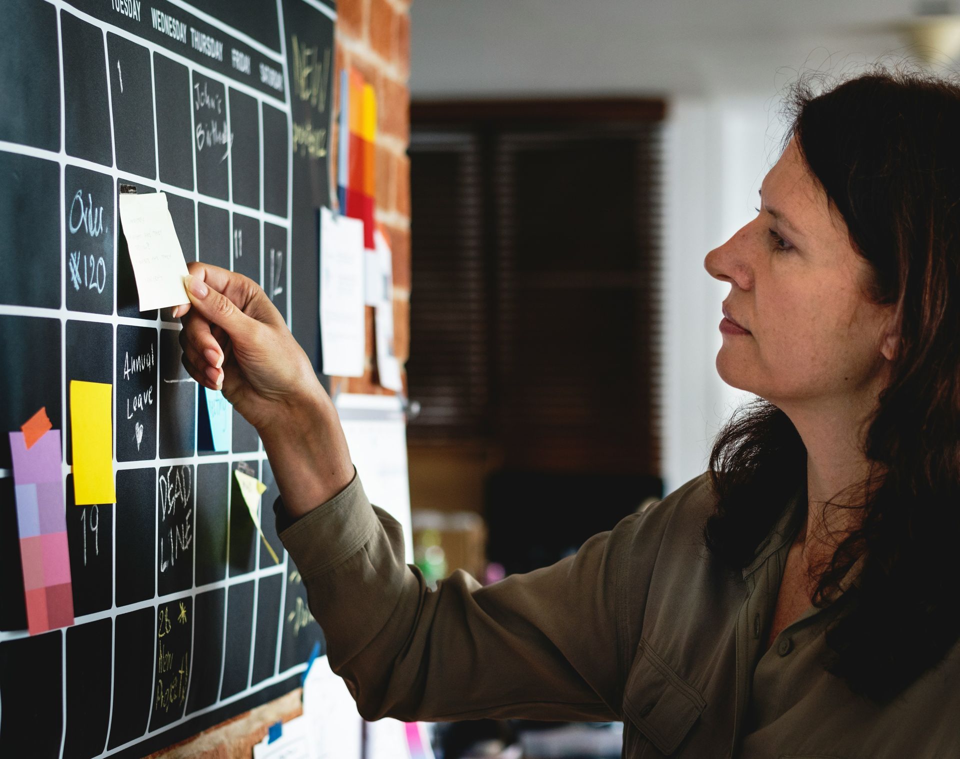 Woman placing a sticky note on a wall of charts and notes during a planning session