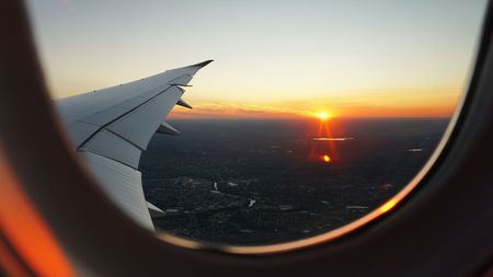 Airplane wing seen through window at sunset over the landscape