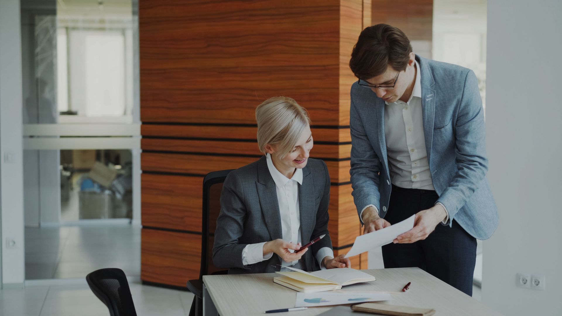 Two professionals review documents at a desk in a modern office.
