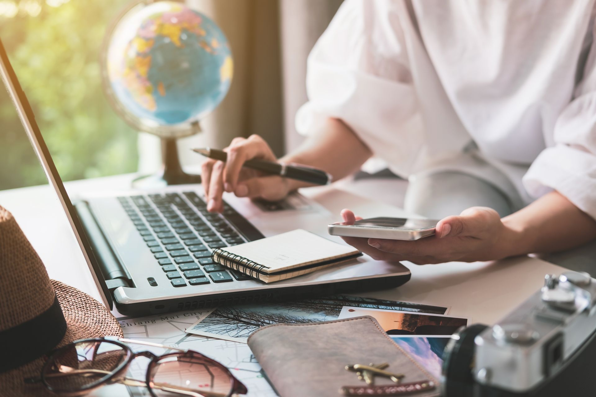 Person working at a laptop beside a notebook and globe on a desk