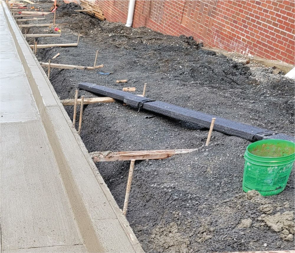 A green bucket is sitting in the dirt next to a brick wall.
