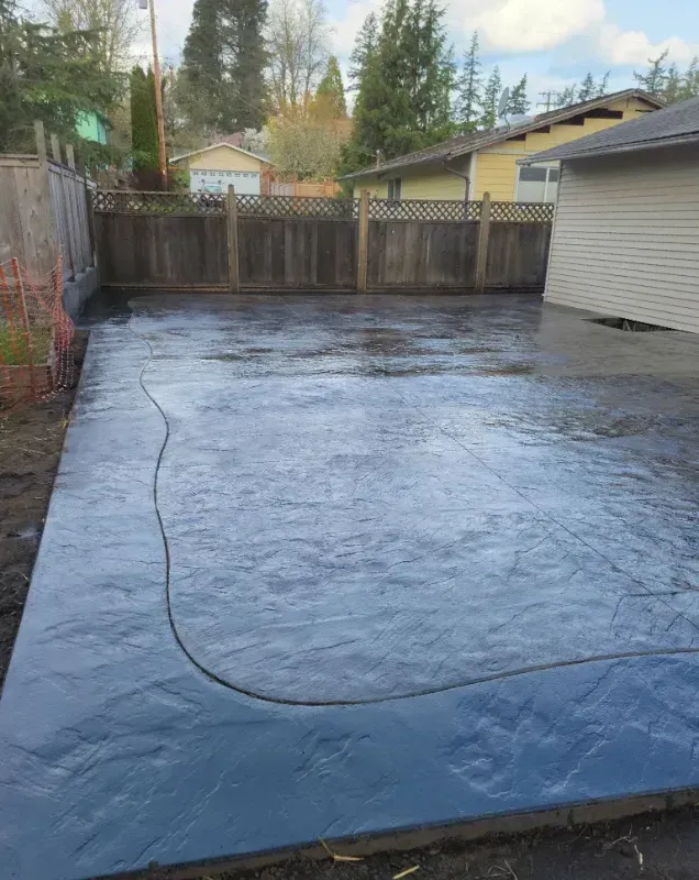 A concrete driveway in a backyard with a fence and a house in the background.