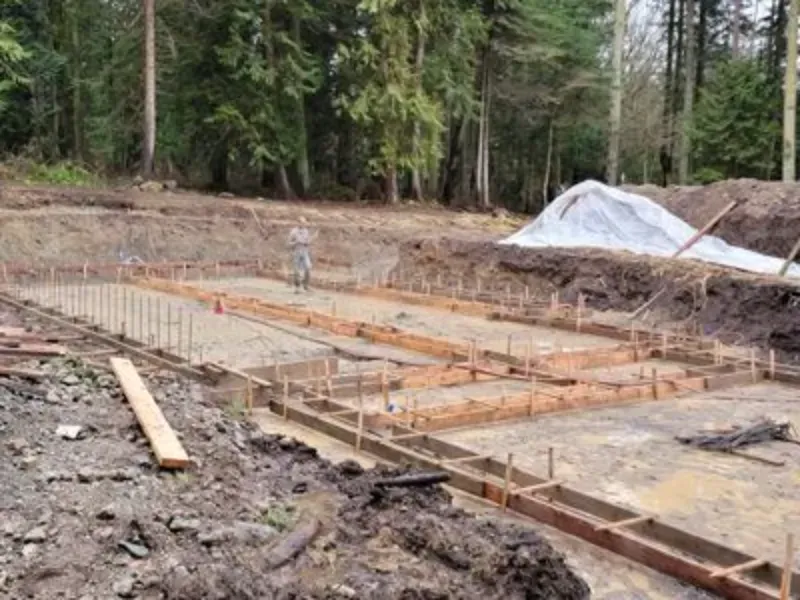 Foundation excavation with rebar and wooden forms in a muddy wooded construction site