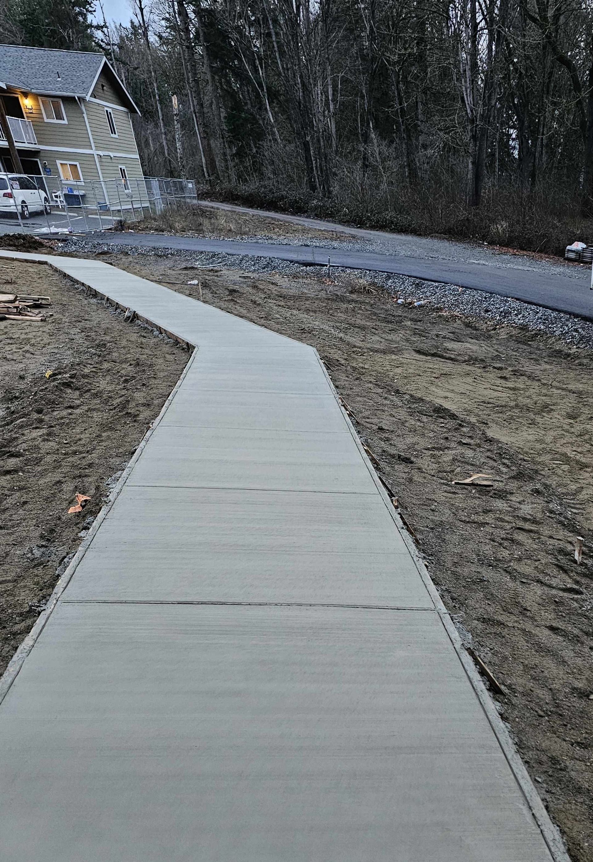 A concrete walkway leading to a house in the woods.