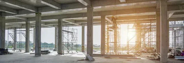 Interior of a concrete building under construction with scaffolding and sunlight.