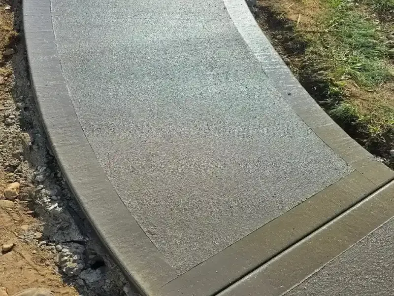 Curved concrete sidewalk with a broom finish texture and smooth border edges during installation.