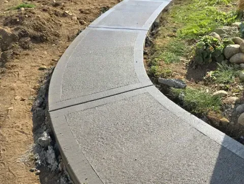 Curved concrete sidewalk bordering dirt and grass.