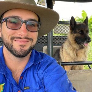 Man in blue shirt and hat smiling beside a tan dog outdoors on a patio — TGT Pty Ltd in Mareeba, QLD