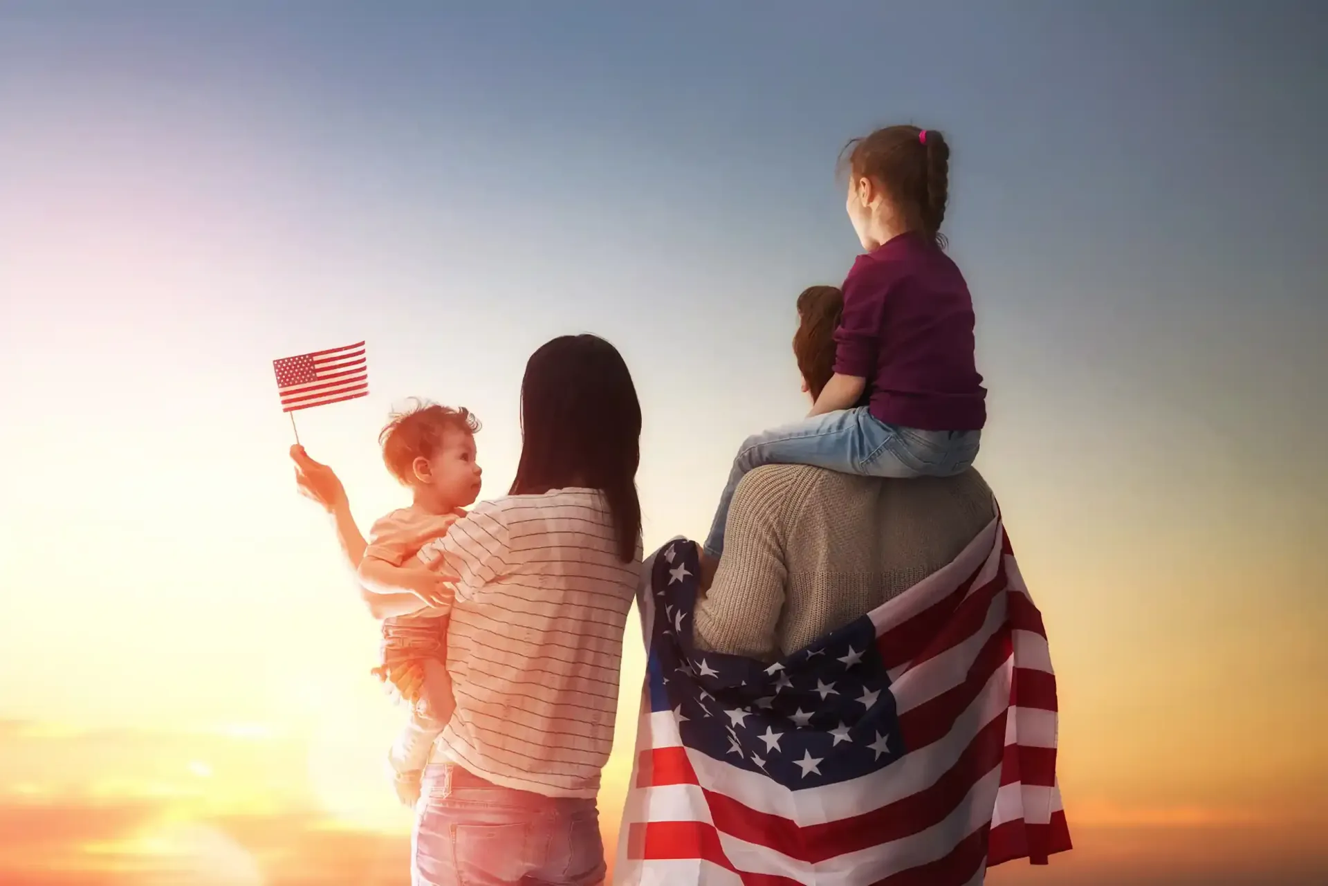 Three people stand at sunset, waving a small U.S. flag beside a larger American flag draped over a horse.