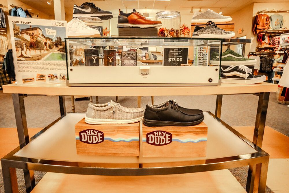 Shoes displayed on a shelf in a store, including Hey Dude shoes on wooden blocks.