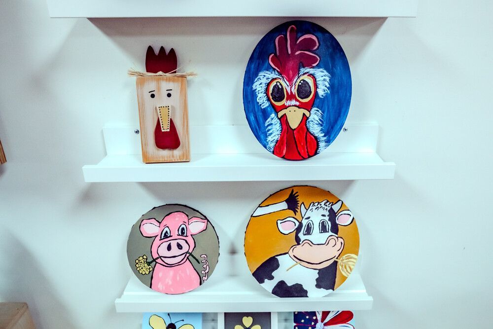 Wooden shelves display folk art: rooster, pig, cow, and a block figure.
