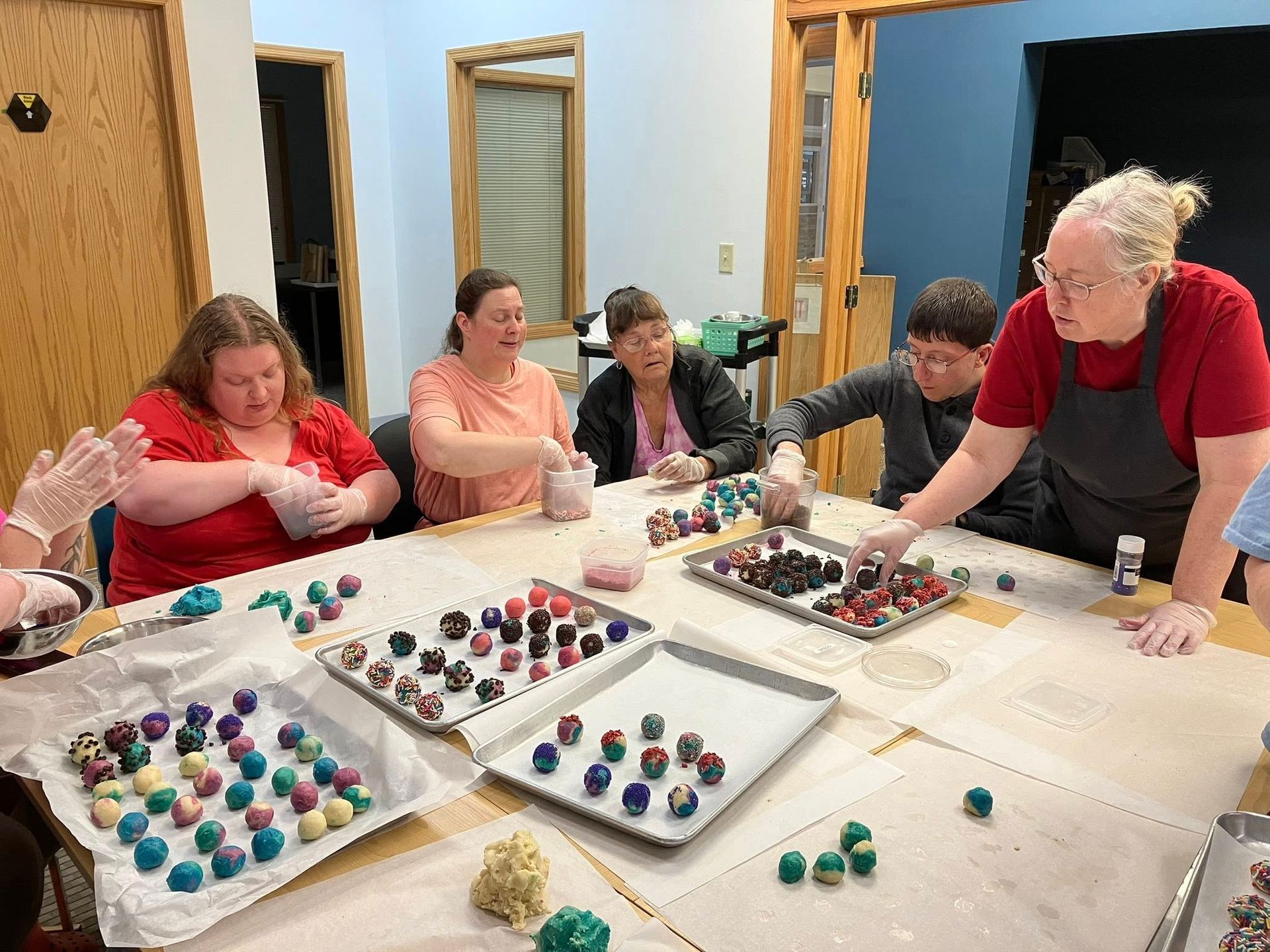 People at a table making colorful treats, likely candy. Several trays of finished items.