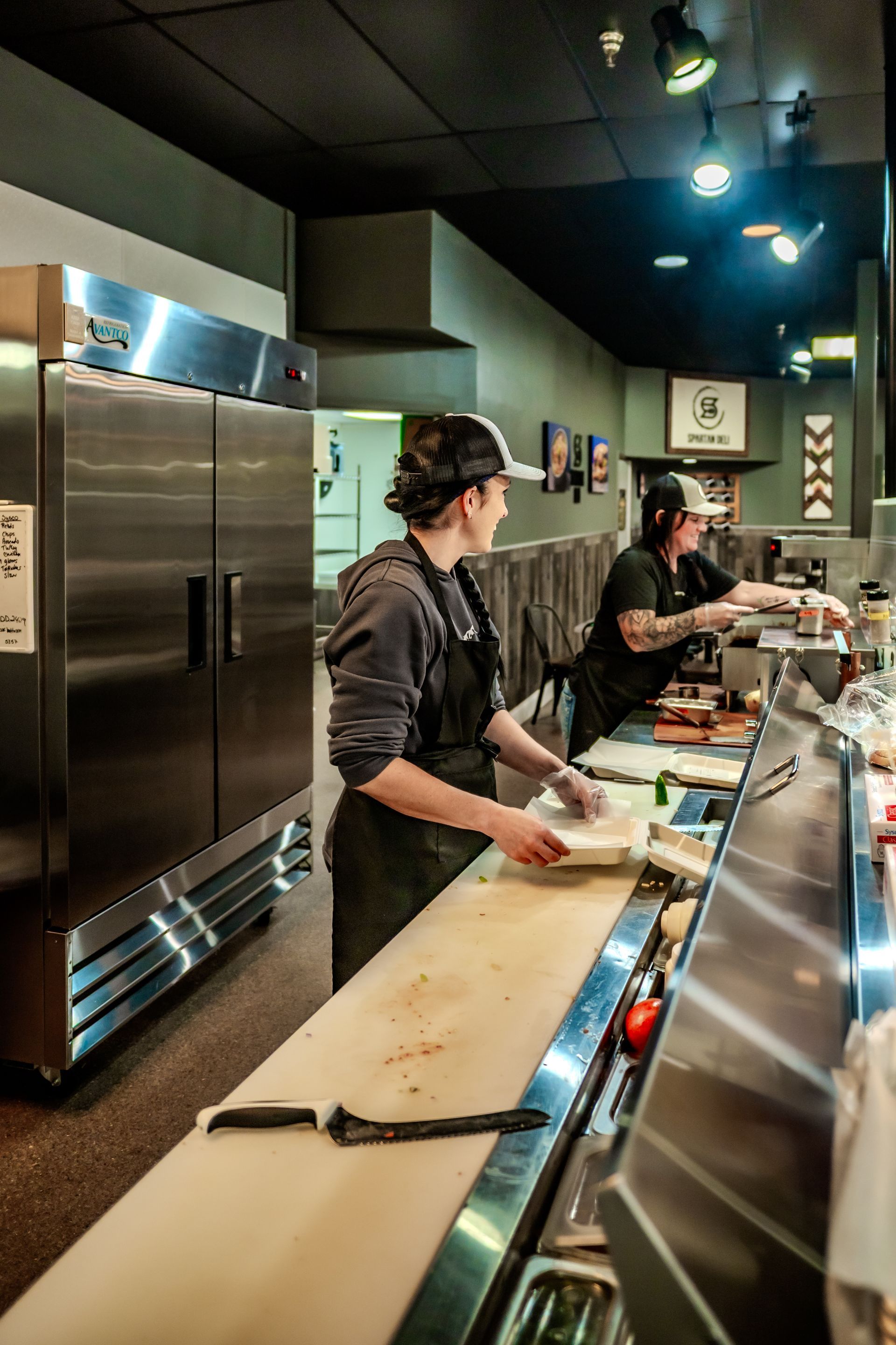 Two people preparing food behind a counter in a restaurant. One person holds a plate.