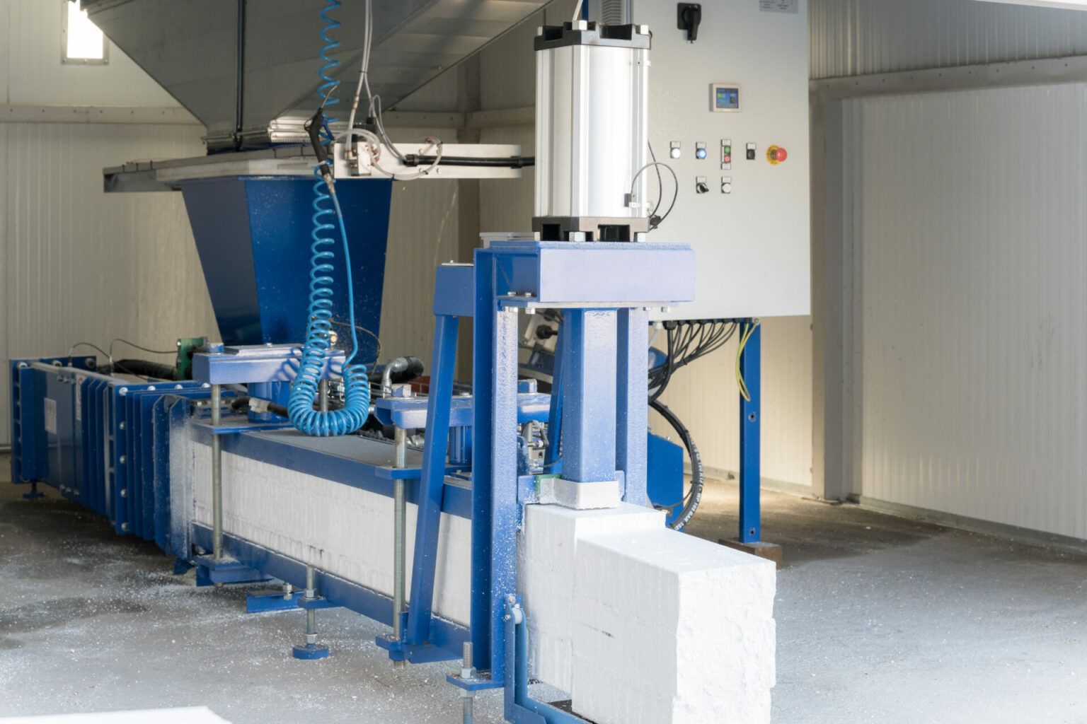 Macchina industriale che produce blocchi di schiuma in fabbrica; schema di colori blu e bianco.