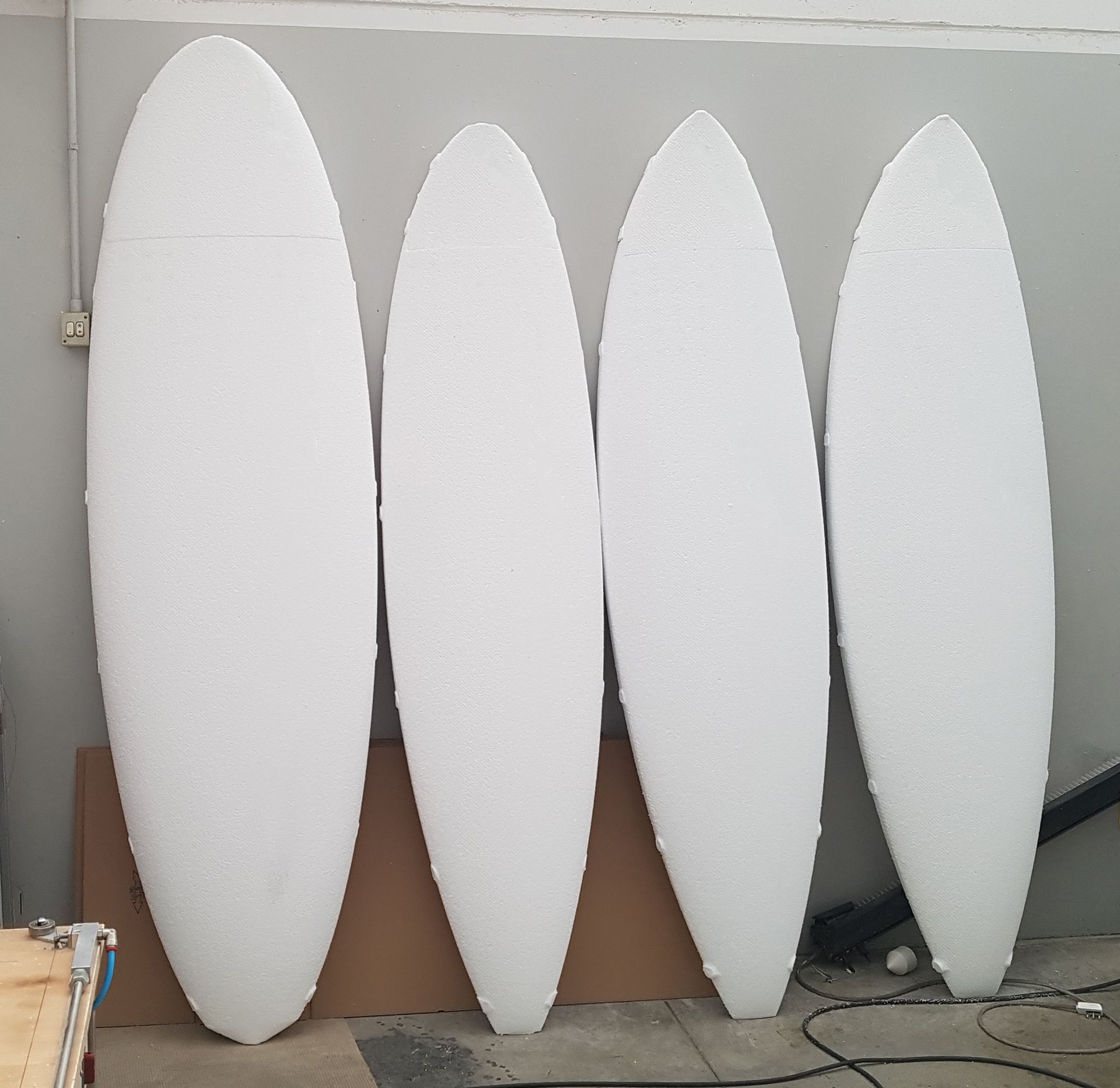 Quattro tavole da surf bianche in schiuma appoggiate a un muro.