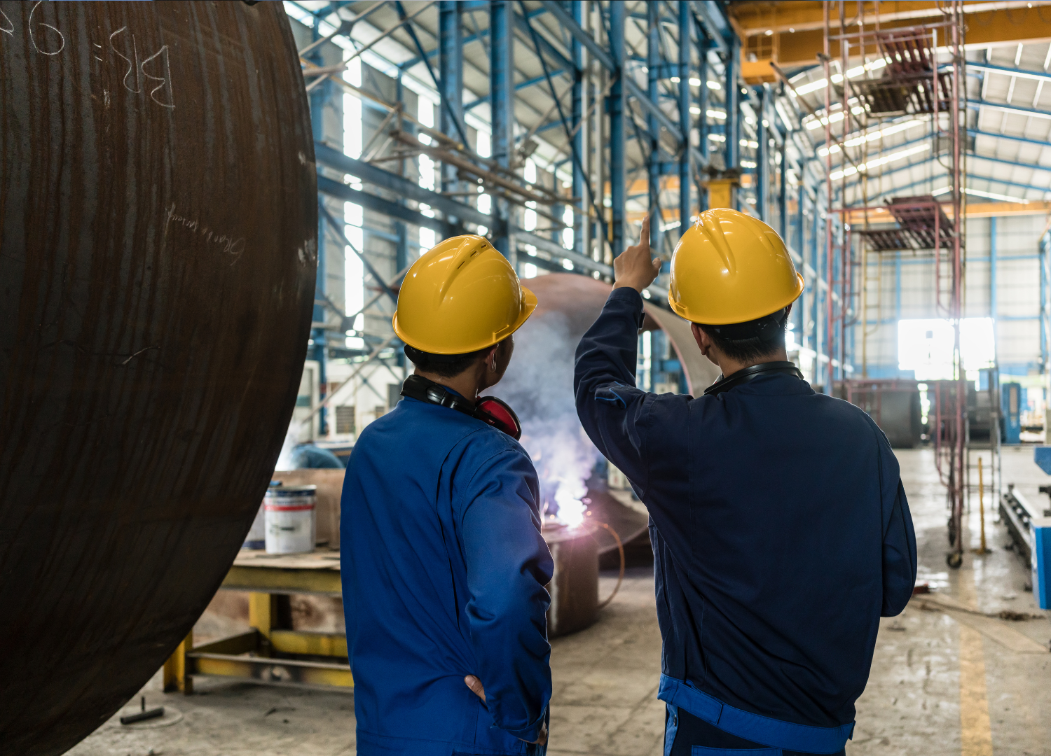 two construction workers are looking at a blueprint in a factory .