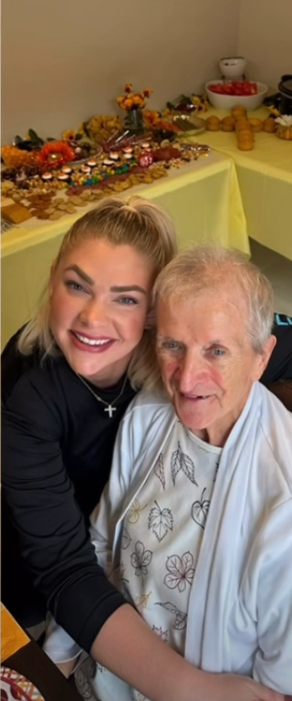 A smiling woman embraces an elderly person indoors at a table decorated with fall-themed table scatter and decor.