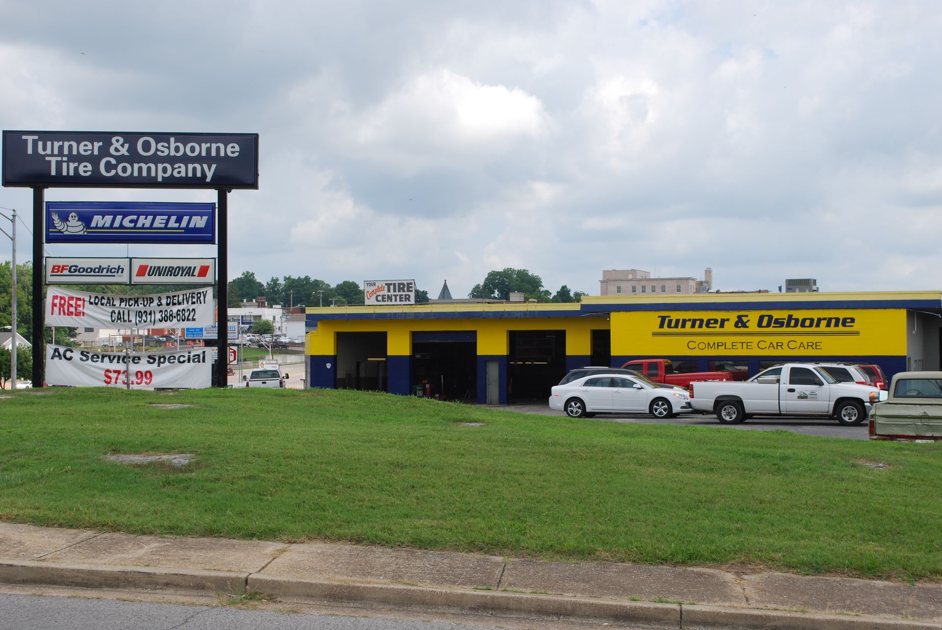 Turner & Osborne Tire Company storefront with yellow facade, parked cars, and roadside sign in front