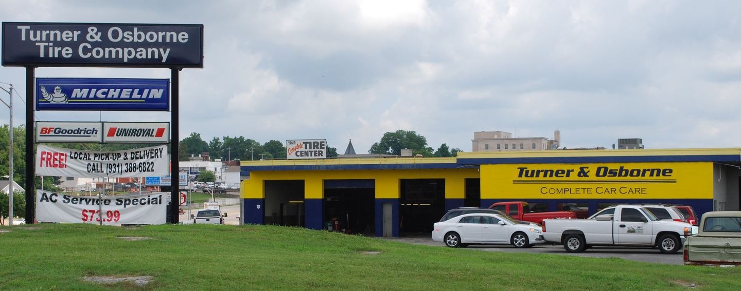 Turner & Osborne Tire Company storefront with yellow awning, parked cars, and roadside sign.