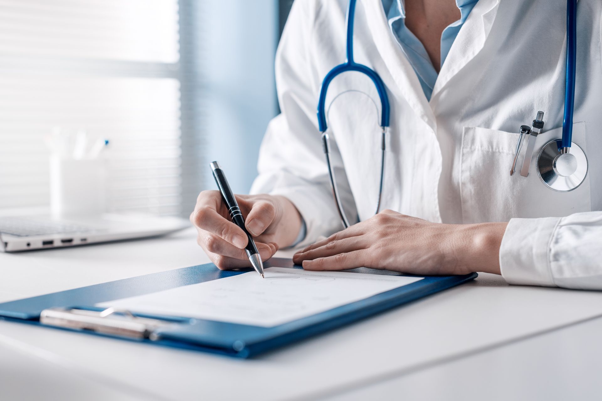 A doctor is writing on a clipboard with a pen.