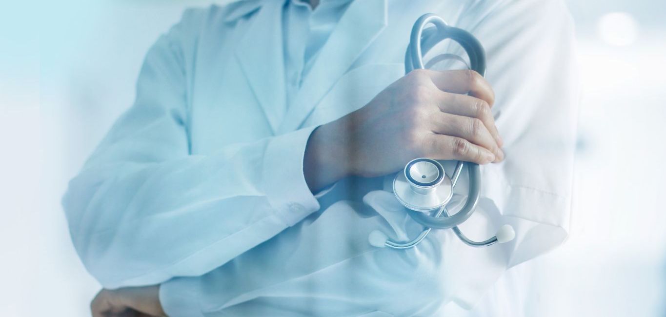 A doctor is holding a stethoscope in a hospital hallway.