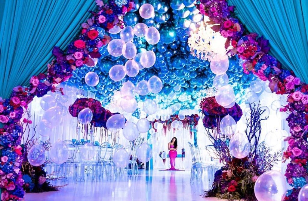 A woman is standing in front of a stage decorated with balloons and flowers.