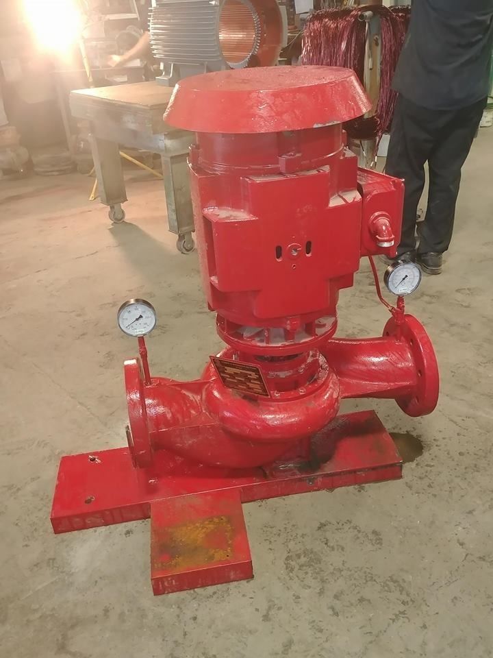 A red pump with two gauges attached to it is sitting on a concrete floor.